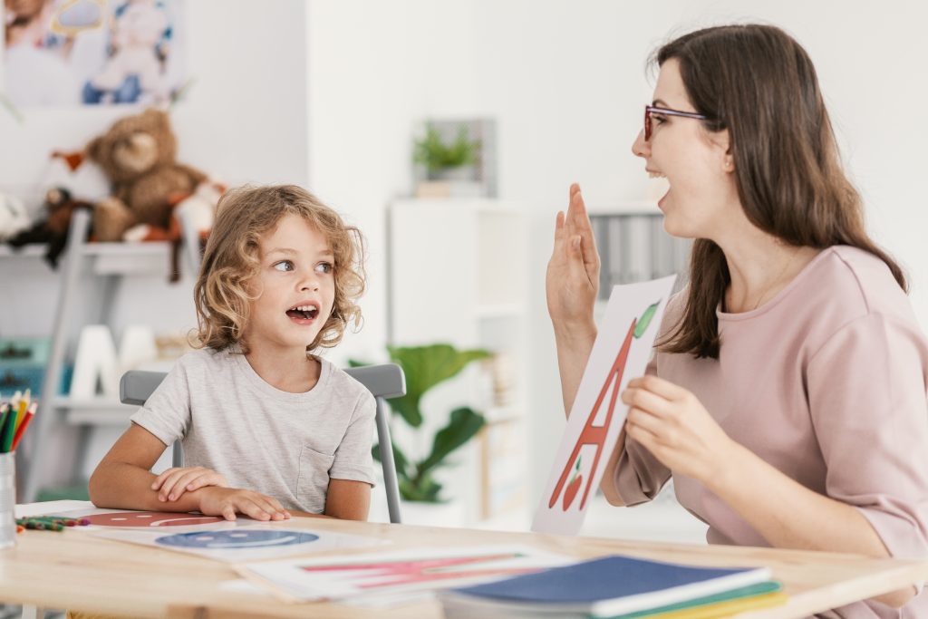 Speech therapist teaching letter pronunciation to a young boy in a classroom